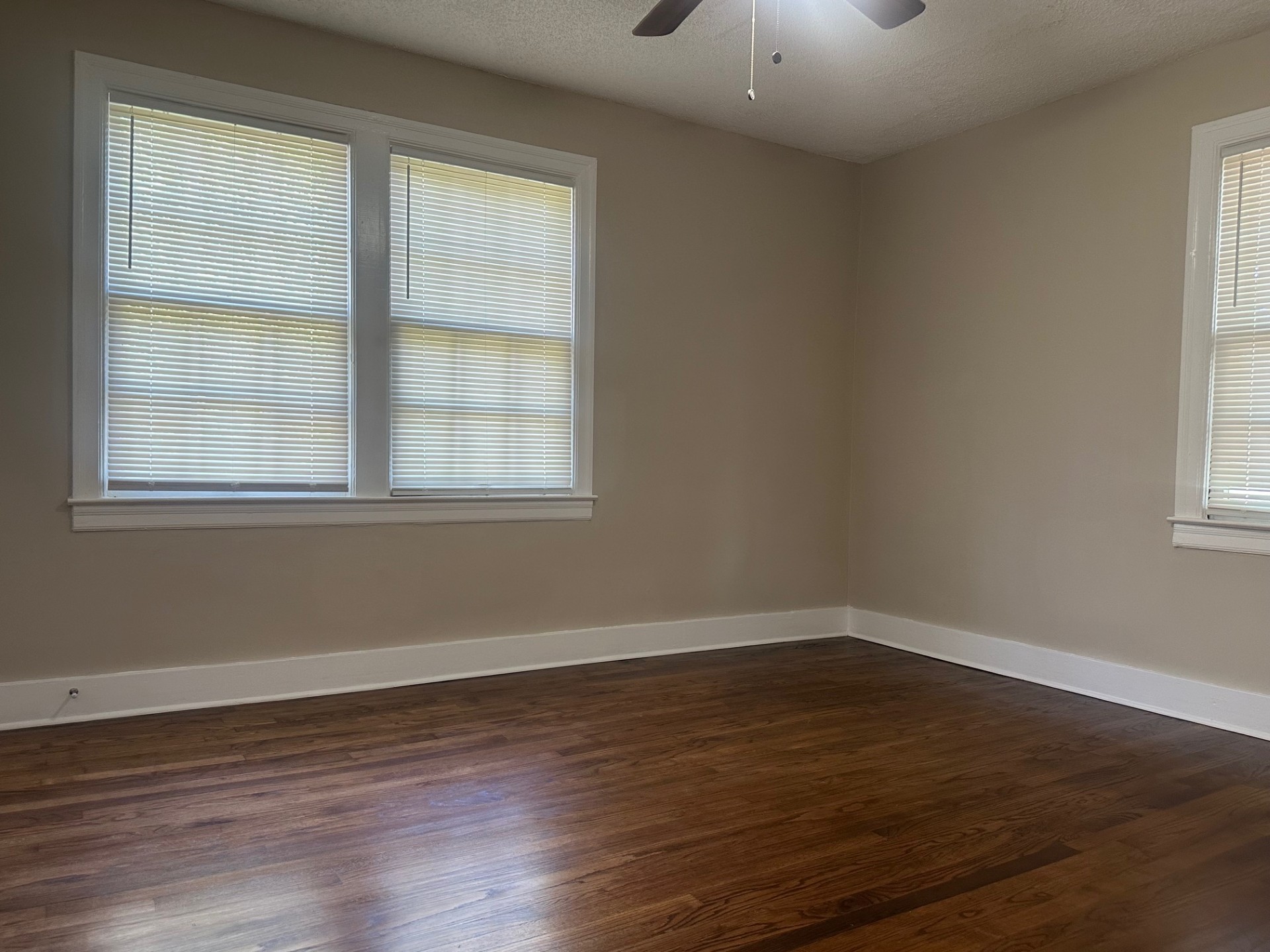 Bedroom with hardwood floors, ceiling fan, and two large windows with blinds